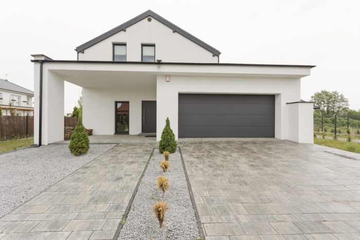 Exterior view of a modern white mansion with a garage and stone driveway